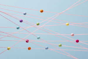 Bunte Kugeln sind durch pinkfarbene Fäden miteinander verbunden und bilden ein Netz vor hellblauem Hintergrund.