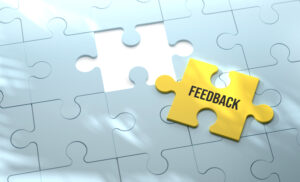 Ein gelbes Puzzleteil mit der Aufschrift „Feedback“ liegt neben einer weißen Puzzlefläche mit einer passenden Lücke.