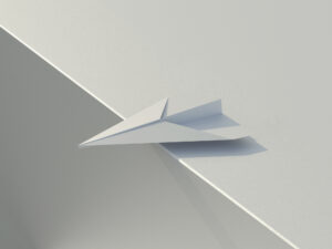 Weißer Papierflieger liegt auf einer Kante und wirft einen klaren Schatten auf die Fläche.
