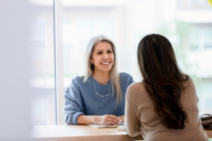 Lehrkraft führt ein Gespräch mit einer Frau in einem hellen Raum.