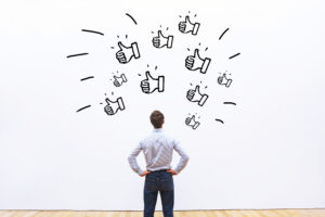 Mann betrachtet eine Wand mit vielen gezeichneten Daumen-hoch-Symbolen als Zeichen von Anerkennung und Wertschätzung.