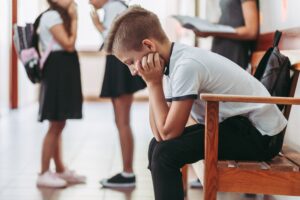Schüler sitzt nachdenklich und mit gesenktem Kopf auf einer Bank im Schulflur.