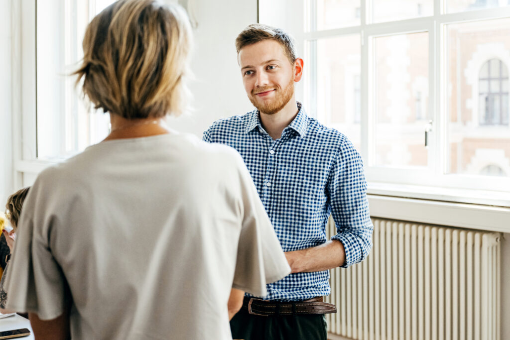Zwei Personen im Gespräch in einem hellen Raum, eine Person im karierten Hemd blickt freundlich.