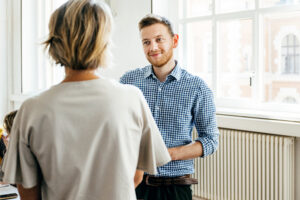 Zwei Personen im Gespräch in einem hellen Raum, eine Person im karierten Hemd blickt freundlich.