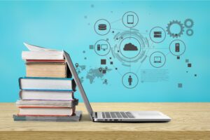 Ein Stapel Bücher steht neben einem aufgeklappten Laptop. Im Hintergrund sind Symbole für digitale Vernetzung, Cloud und Technologie zu sehen.