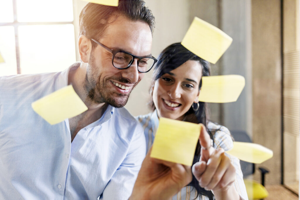 Zwei Personen arbeiten gemeinsam an einer Glaswand mit Haftnotizen und entwickeln Ideen für Schule und Bildung.