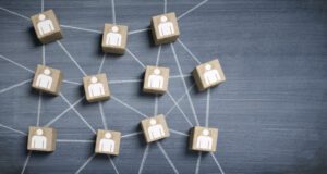 Mehrere Holzwürfel mit Symbolen von Personen darauf liegen auf einer Tafel. Die Würfel sind durch weiße Linien miteinander verbunden und symbolisieren ein Netzwerk.