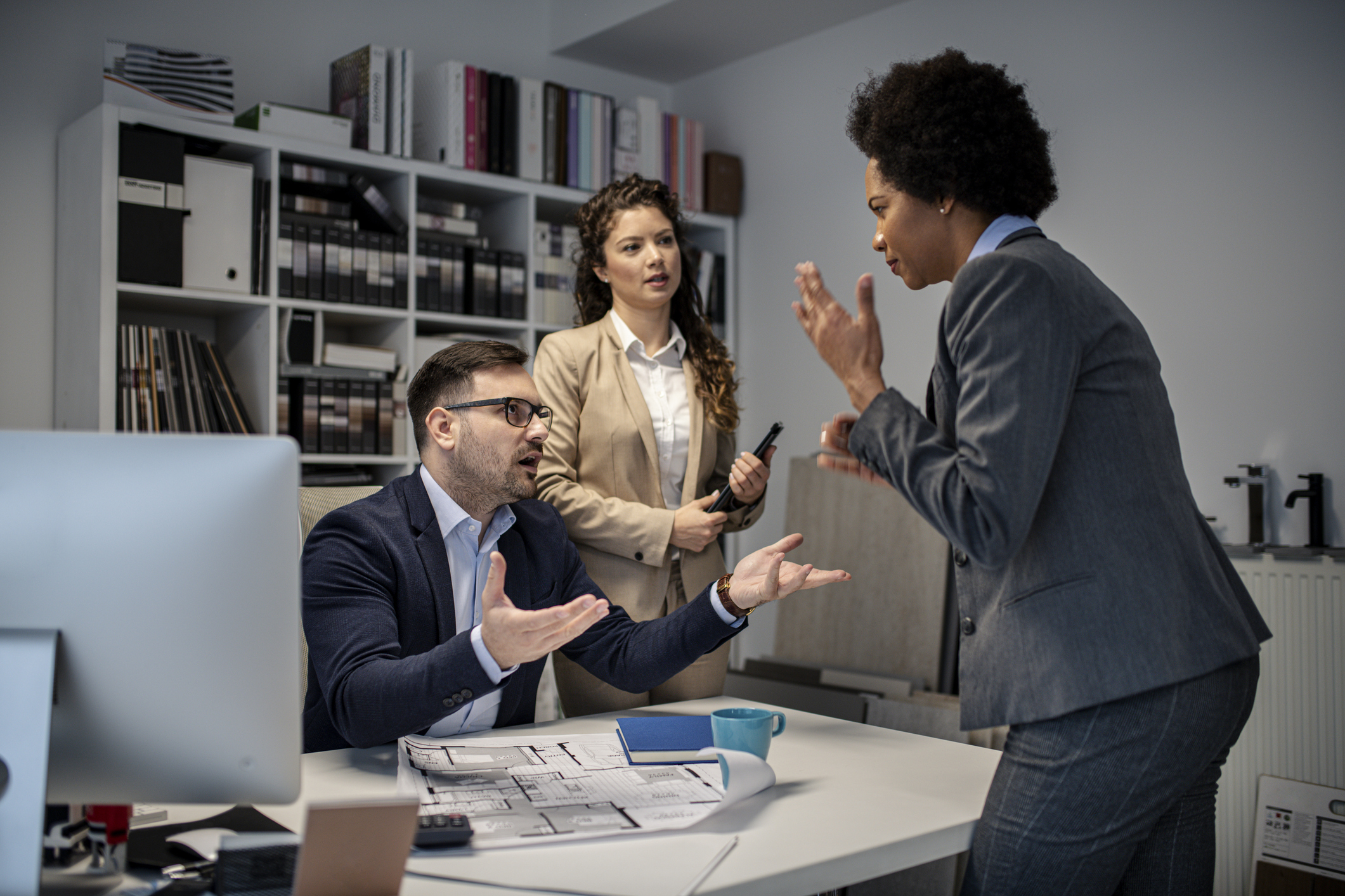 Drei Personen in einem Büro im Gespräch, zwei diskutieren gestikulierend, eine hört zu. Drei Personen in einem Büro im Gespräch, zwei diskutieren gestikulierend, eine hört zu.