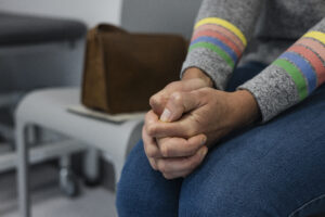 Nahaufnahme einer Person im Wartezimmer, die nervös die Hände verschränkt.