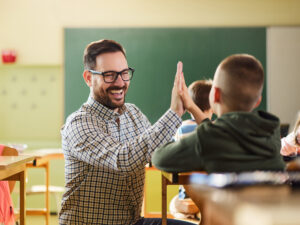 Ein Lehrer und ein Schüler geben sich im Klassenzimmer lächelnd ein High-Five.
