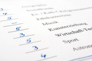 Nahaufnahme eines Bewertungsbogens mit Noten in blauer Tinte, die neben den Fächern wie Musik, Kunst und Wirtschaft-Technik aufgeführt sind.