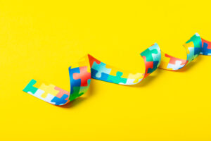 Ein schmales, geschwungenes Band mit buntem Puzzle-Muster liegt auf einem kräftig gelben Hintergrund und wirft einen weichen Schatten.