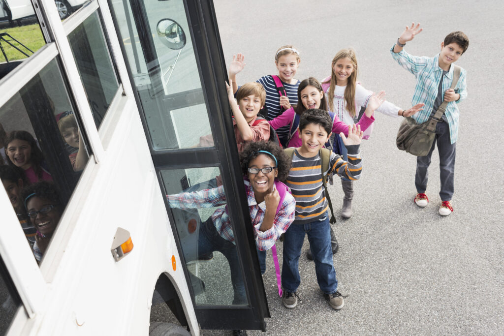 Eine Gruppe von Kindern steht in freudiger Erwartung auf die Klassenfahrt an einem Bus.