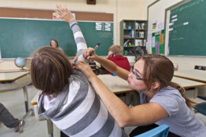 Eine Schülerin malt ihren Mitschüler während des Unterrichts mit einem Stift an.