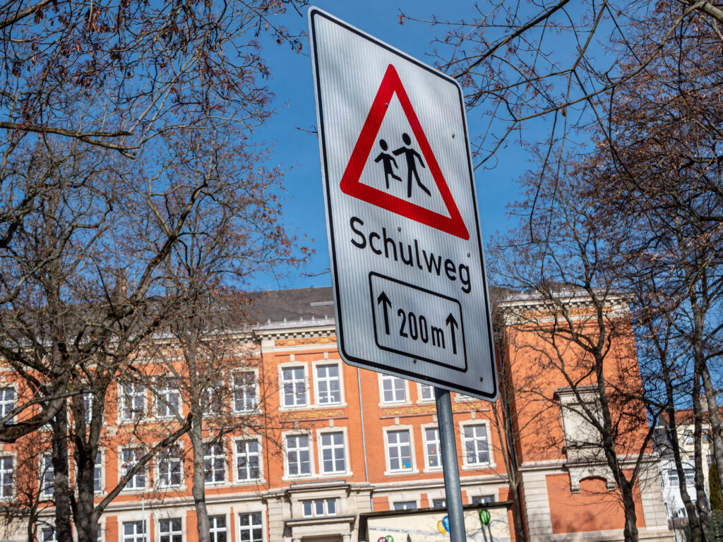 Das Bild zeigt ein Warnschild "Schulweg" am Straßenrand