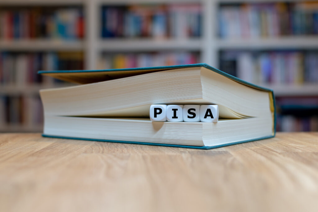 ISA-Studie: Buch mit Buchstabenwürfeln „PISA“ vor einem Bücherregal